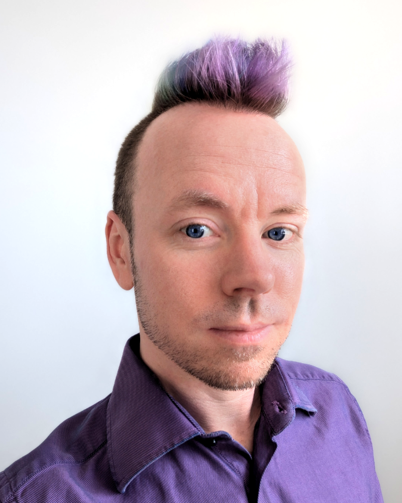 Headshot of a white man in a purple dress shirt and sporting a purple mohawk.